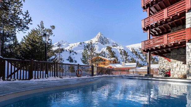 A swimming pool with a wooden deck, surrounded by snow-covered mountains and trees. - Arc 1950 - Apartment 4 people, ski-in/ski-out, wellness included (Les Arcs 1950)