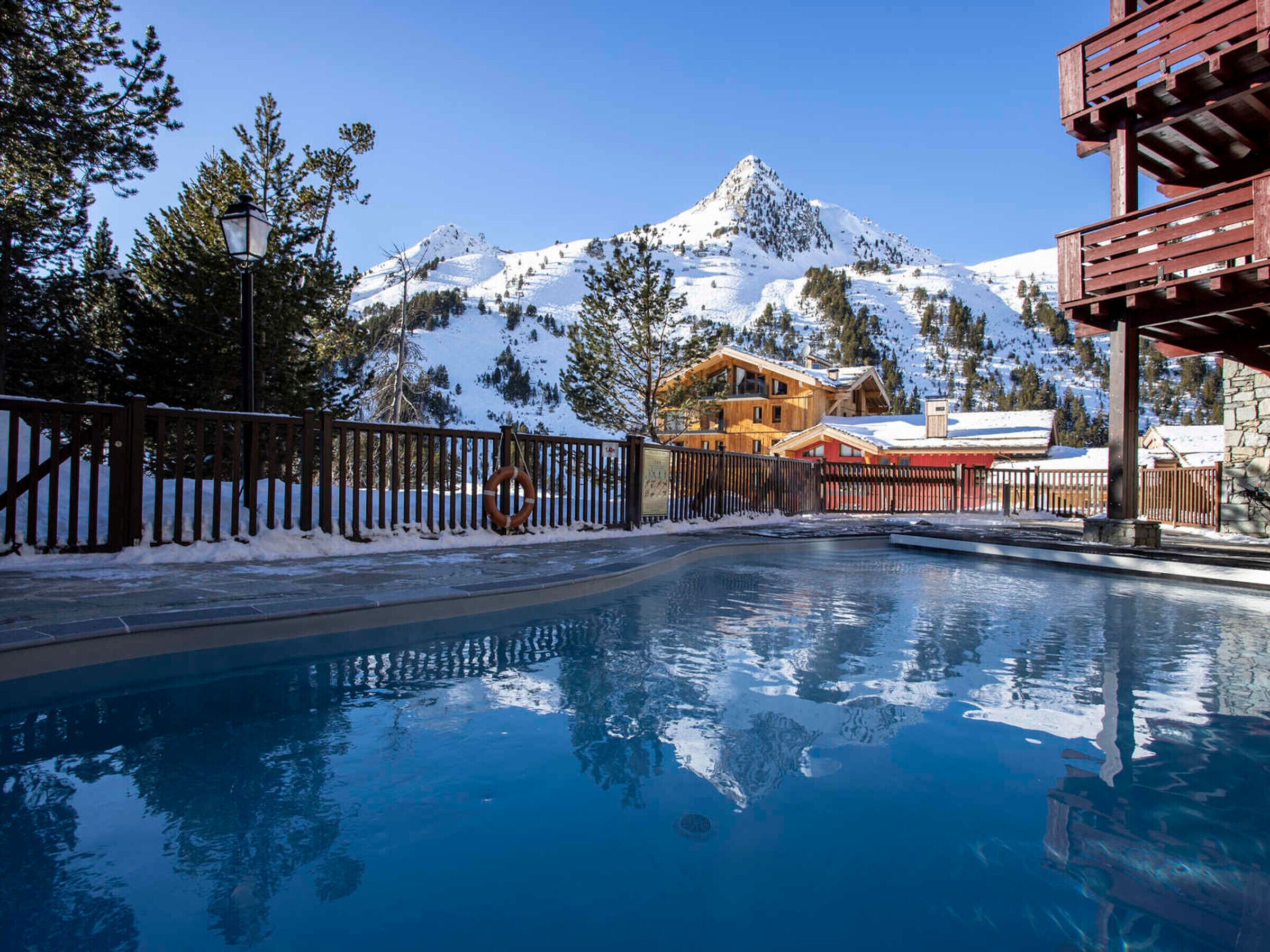 Un espace piscine doté d’une terrasse en bois, d’une bouée de sauvetage et offrant une vue sur les montagnes.