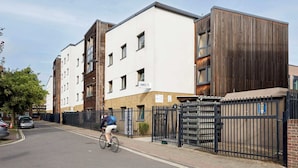 A modern apartment building with a mix of white and wooden facades, a gated entrance, and a cyclist on the street. - Students Only - Central London Student Accommodation (London)