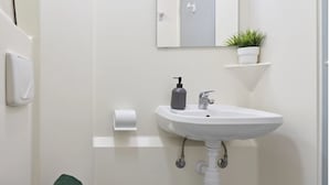 A bathroom with a white sink, a hand soap dispenser, a toilet paper holder, and a potted plant on a shelf. - Students Only - Central London Student Accommodation (London)