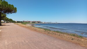 A coastal road with a clear sky, a sandy beach, and buildings in the background.