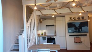 A compact kitchen with white cabinets, a wooden table, and a staircase leading to another level.