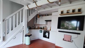 A compact living space with a wooden table, a TV mounted on the wall, and a staircase leading to an upper level.