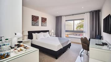 Una habitación de hotel moderna con una cama grande, un escritorio con silla, un televisor y una ventana con cortinas.
