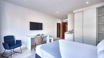 A modern hotel room with a large bed, a desk, a chair, a TV mounted on the wall, and a wardrobe.