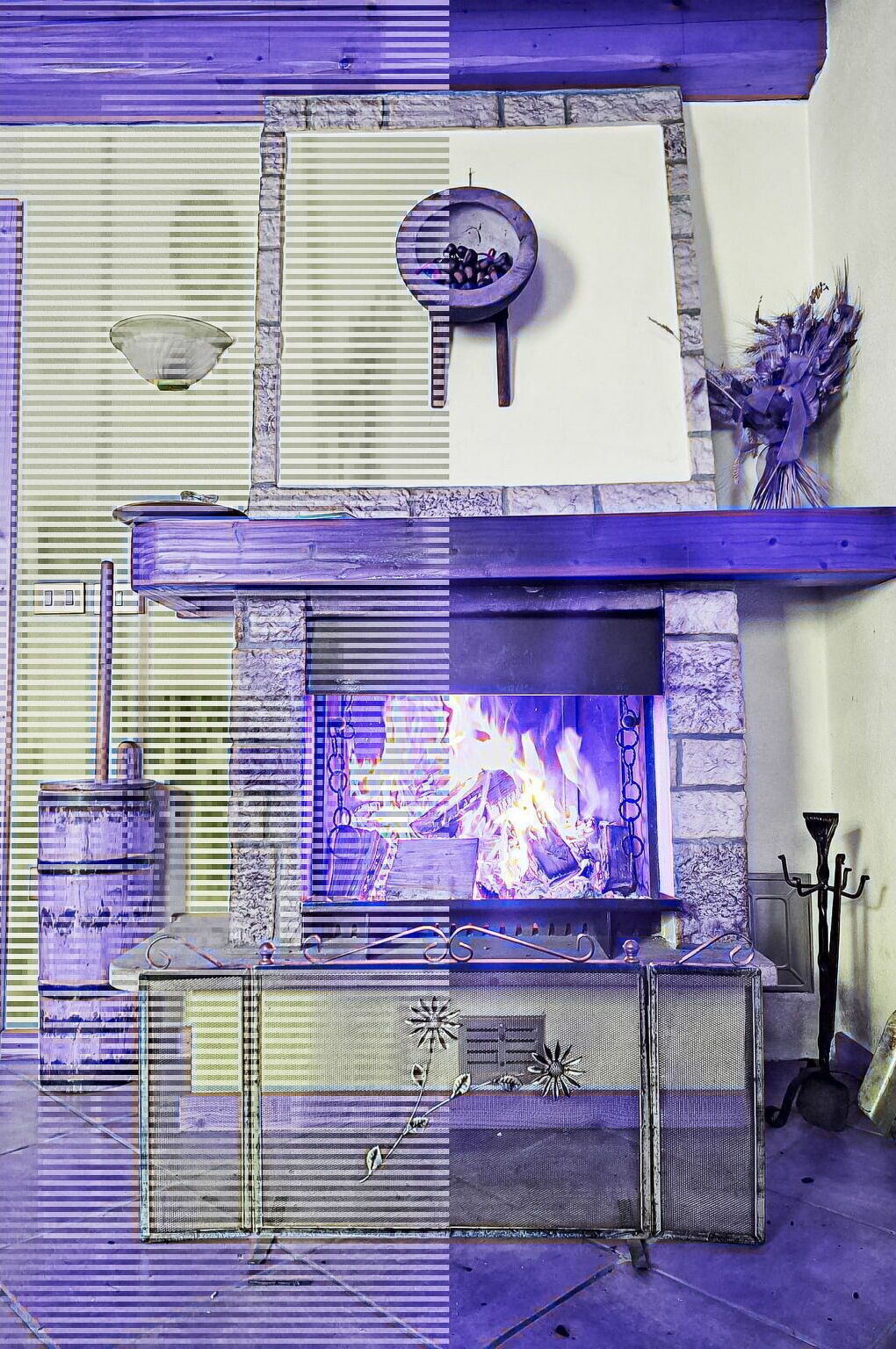 A fireplace with a stone surround, a mantel with a bowl and a candelabra, and a decorative vase with dried flowers.