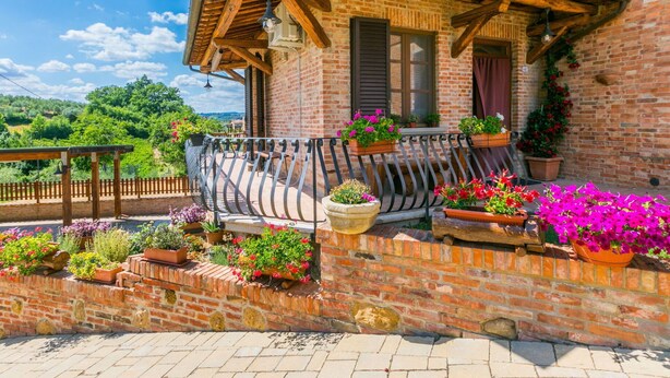 A brick building with a wooden balcony, potted plants, and an air conditioning unit. - Nice apartment for 3 guests with A/C, WIFI, patio and pets allowed (Montepulciano)