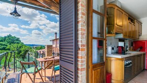 A balcony with a wooden railing, a table with chairs, and a view of greenery and buildings in the distance. - Nice apartment for 3 guests with A/C, WIFI, patio and pets allowed (Montepulciano)