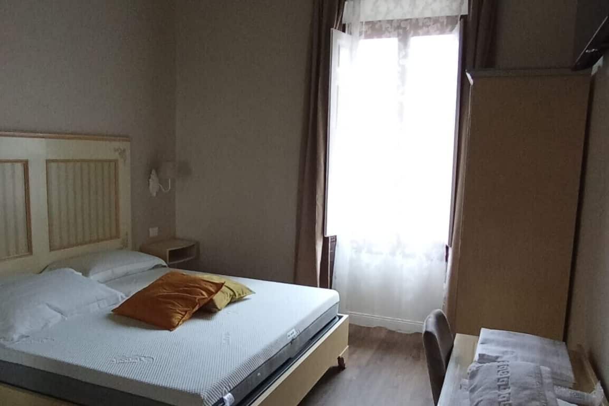 Ein Schlafzimmer mit Bett, Nachttisch, Kommode und einem Fenster mit Vorhängen.