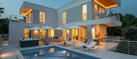 A modern two-story house with a swimming pool, outdoor seating, and a hot tub.