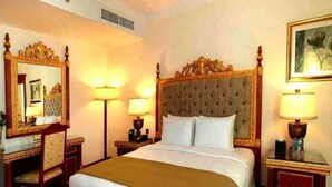 Une chambre d’hôtel avec un grand lit, une commode en bois, deux tables de chevet avec des lampes, un miroir et un tableau encadré au mur.