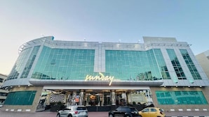 Un hôtel moderne à la façade incurvée, doté de grandes fenêtres en verre et d’un panneau néon bien visible sur lequel on peut lire « Sunday Hotel ».