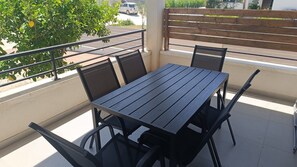 A balcony with a table and chairs, a railing, and a view of a parking area and greenery.