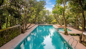 A rectangular pool with a tiled bottom, surrounded by trees and a stone wall. - The Orchid Rishivan Rishikesh (Rishikesh)
