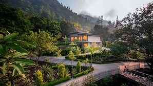 A two-story stone building with a balcony, surrounded by lush greenery and a mountainous backdrop. - The Orchid Rishivan Rishikesh (Rishikesh)