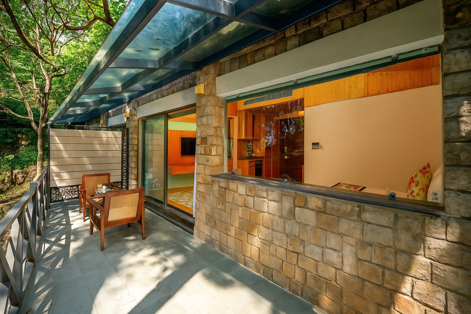 A covered outdoor seating area with a stone wall and glass doors leading to a room.