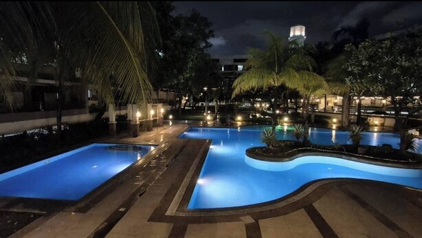 A nighttime swimming pool area with multiple pools, palm trees, and a water tower in the background. - Jewel's Homey Place -2br in a Resort-like Condo (Pasig)