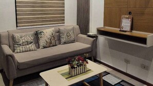 A living room with a sofa, coffee table, and a wall-mounted shelf. - Jewel's Homey Place -2br in a Resort-like Condo (Pasig)