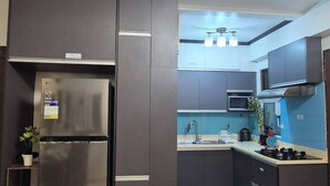 A modern kitchen with dark cabinets, a stainless steel refrigerator, and a microwave. - Jewel's Homey Place -2br in a Resort-like Condo (Pasig)