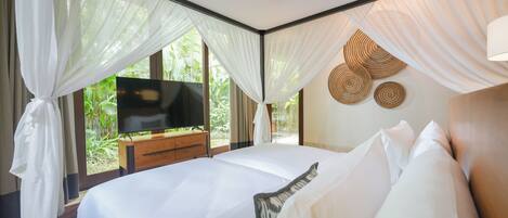 A bedroom with a large bed, a TV, and a view of greenery outside.