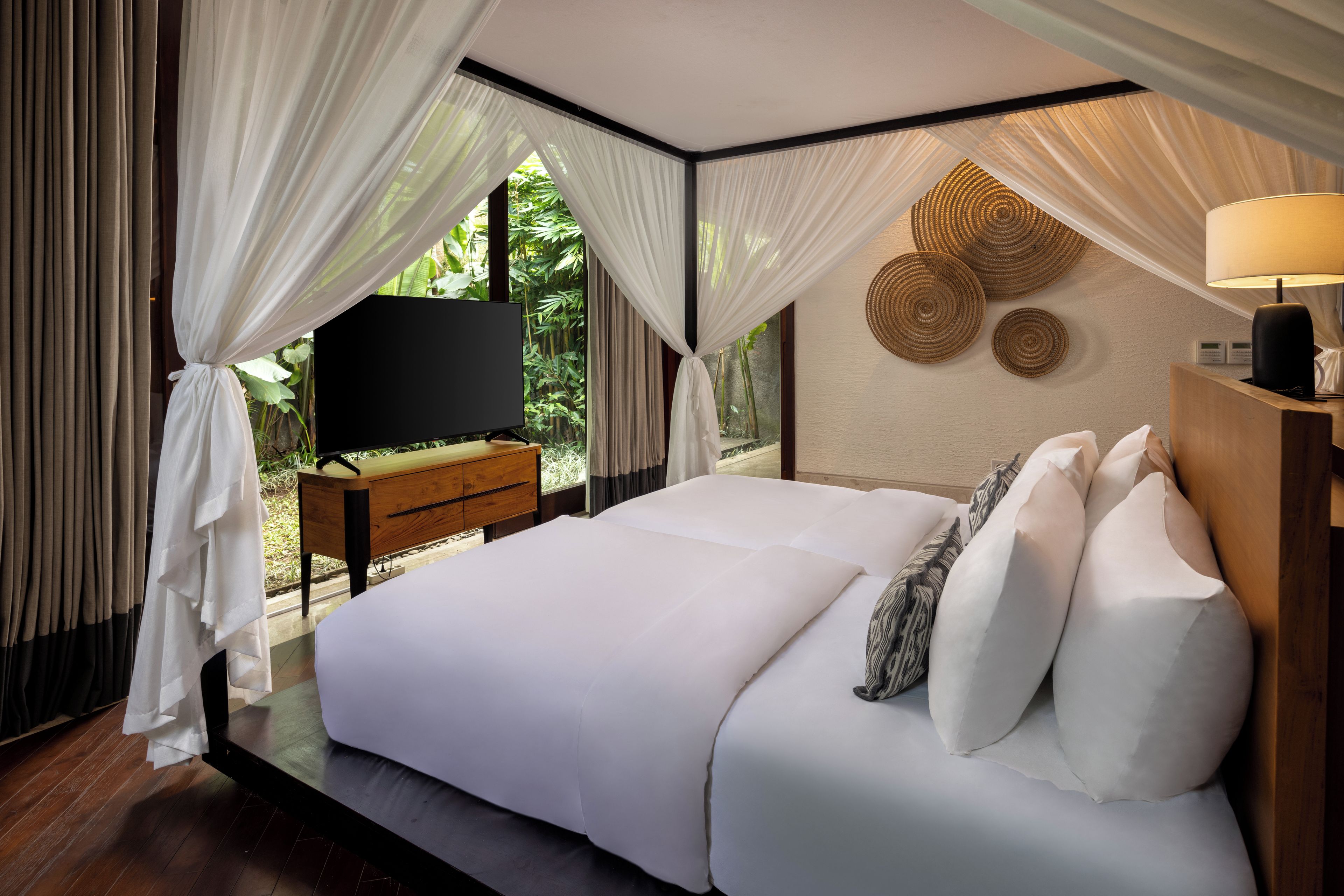 Una camera da letto con un letto grande, un comodino in legno, una TV e vista sul verde dalla finestra.