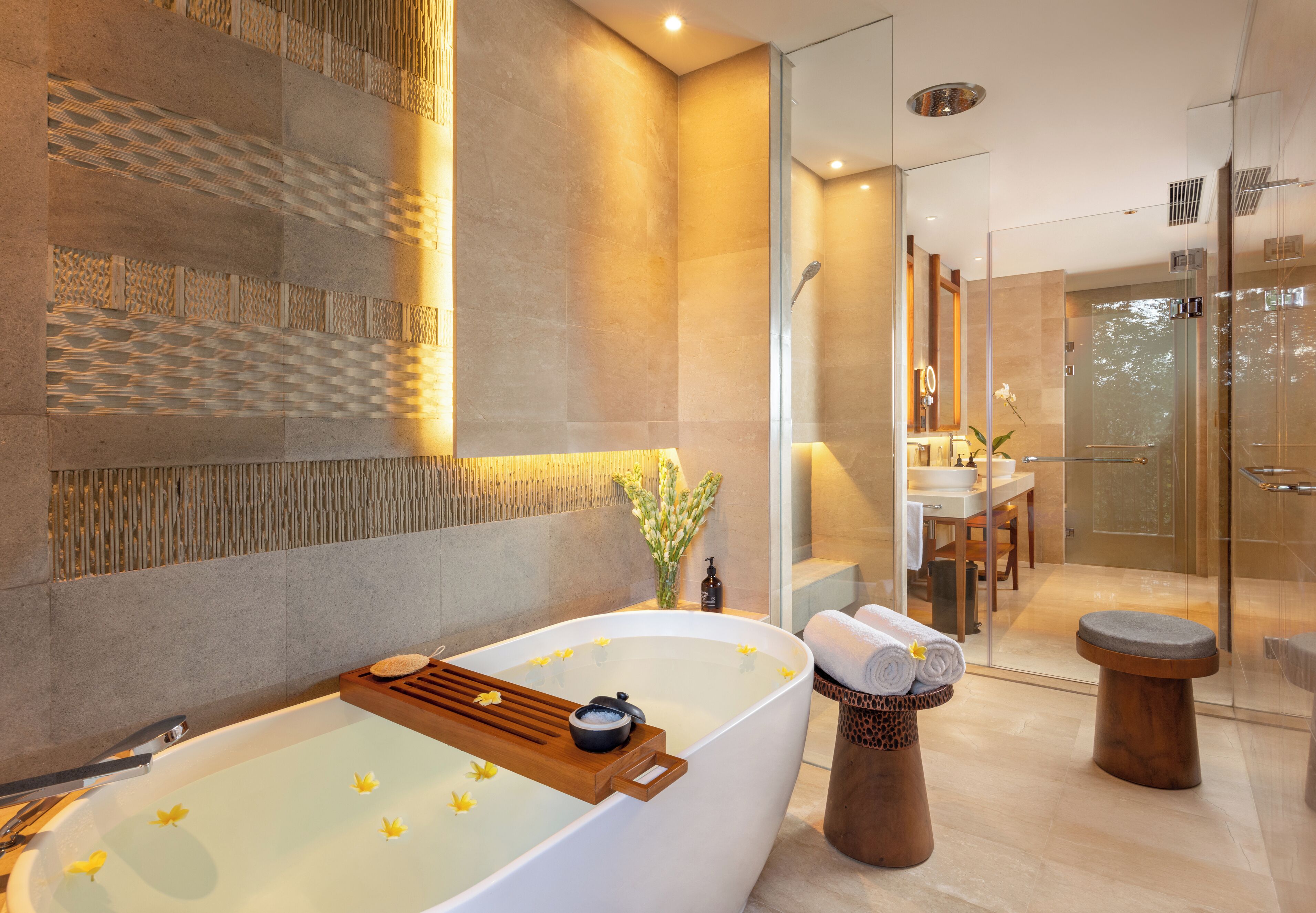 A modern bathroom with a large bathtub, a glass shower enclosure, and a wooden side table with towels.