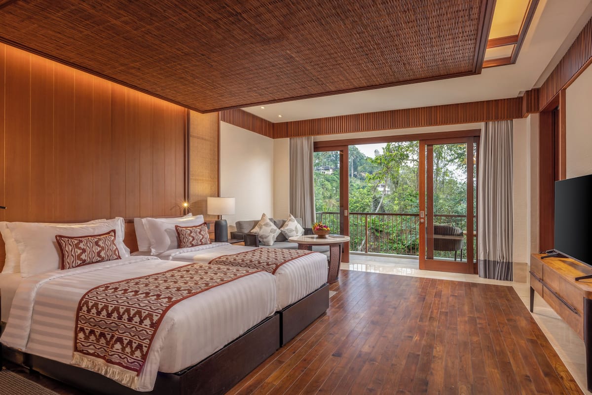 Habitación de hotel con una cama grande, televisión, balcón con vistas a zonas verdes y techo de madera.