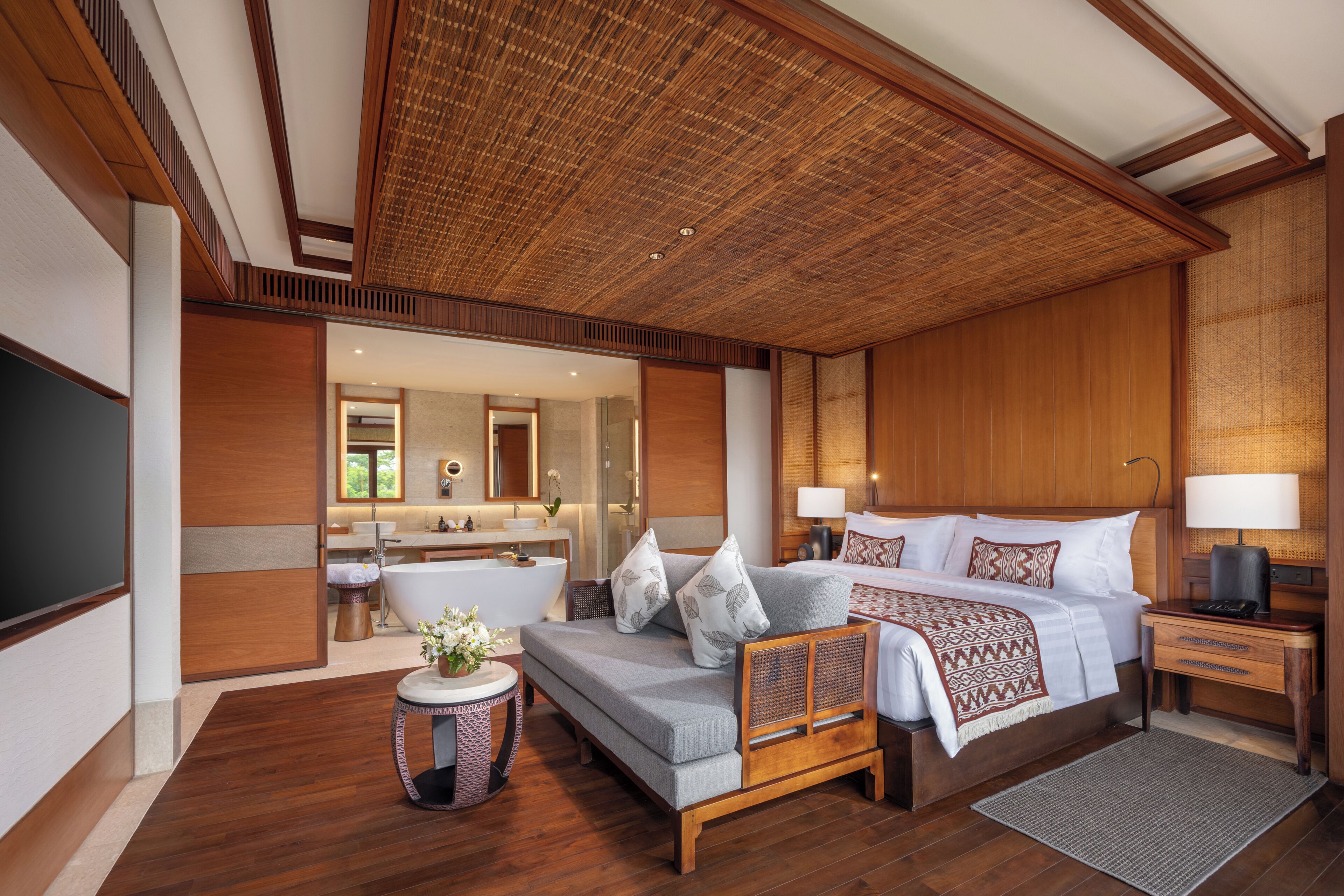 A spacious bedroom with a large bed, a sofa, a small round table with a plant, and a separate bathroom visible through an open door.