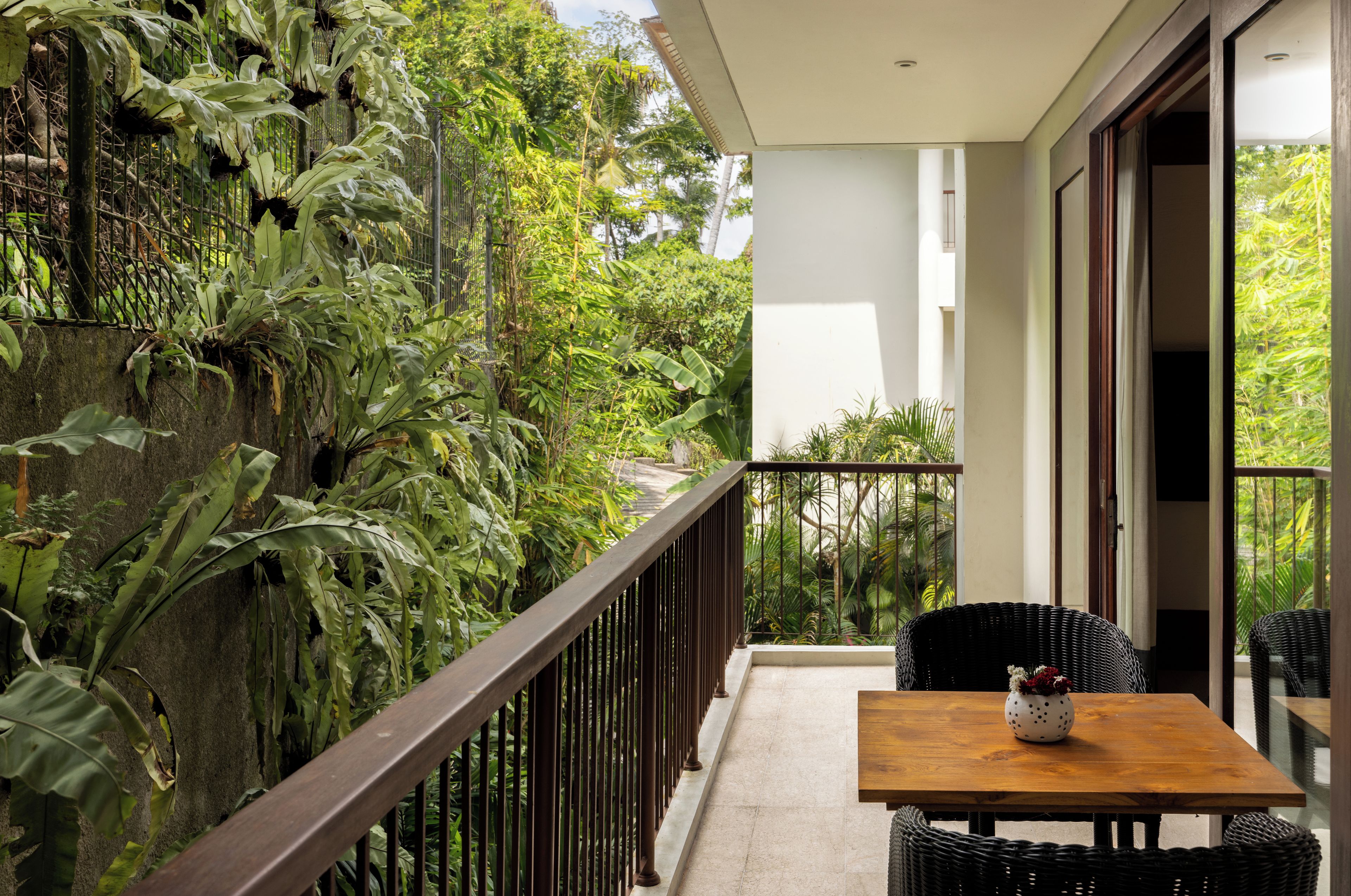 A balcony with a wooden table and chairs, surrounded by lush greenery.