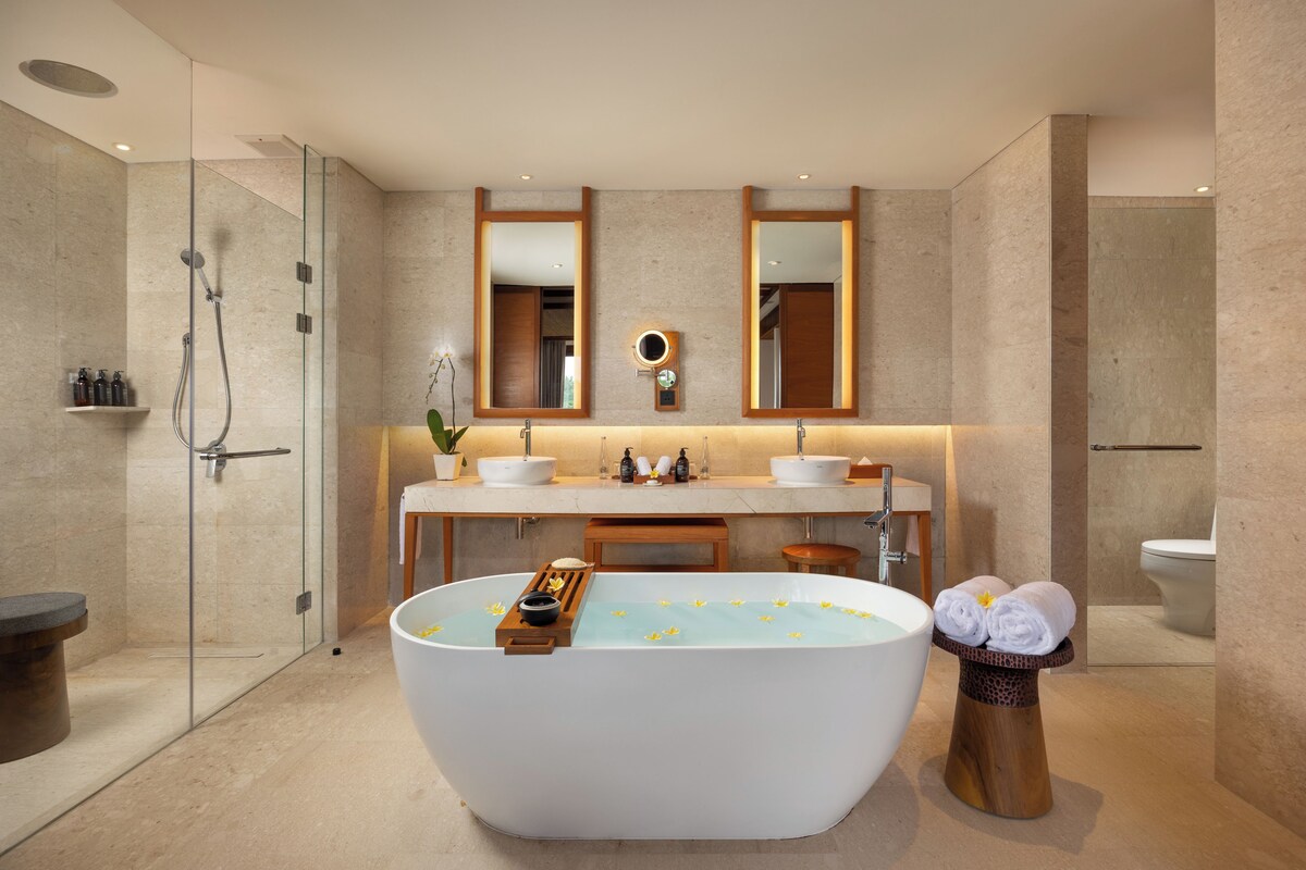 Een moderne badkamer met een vrijstaand bad, een douche met glazen wanden en een wastafel met twee wasbakken.