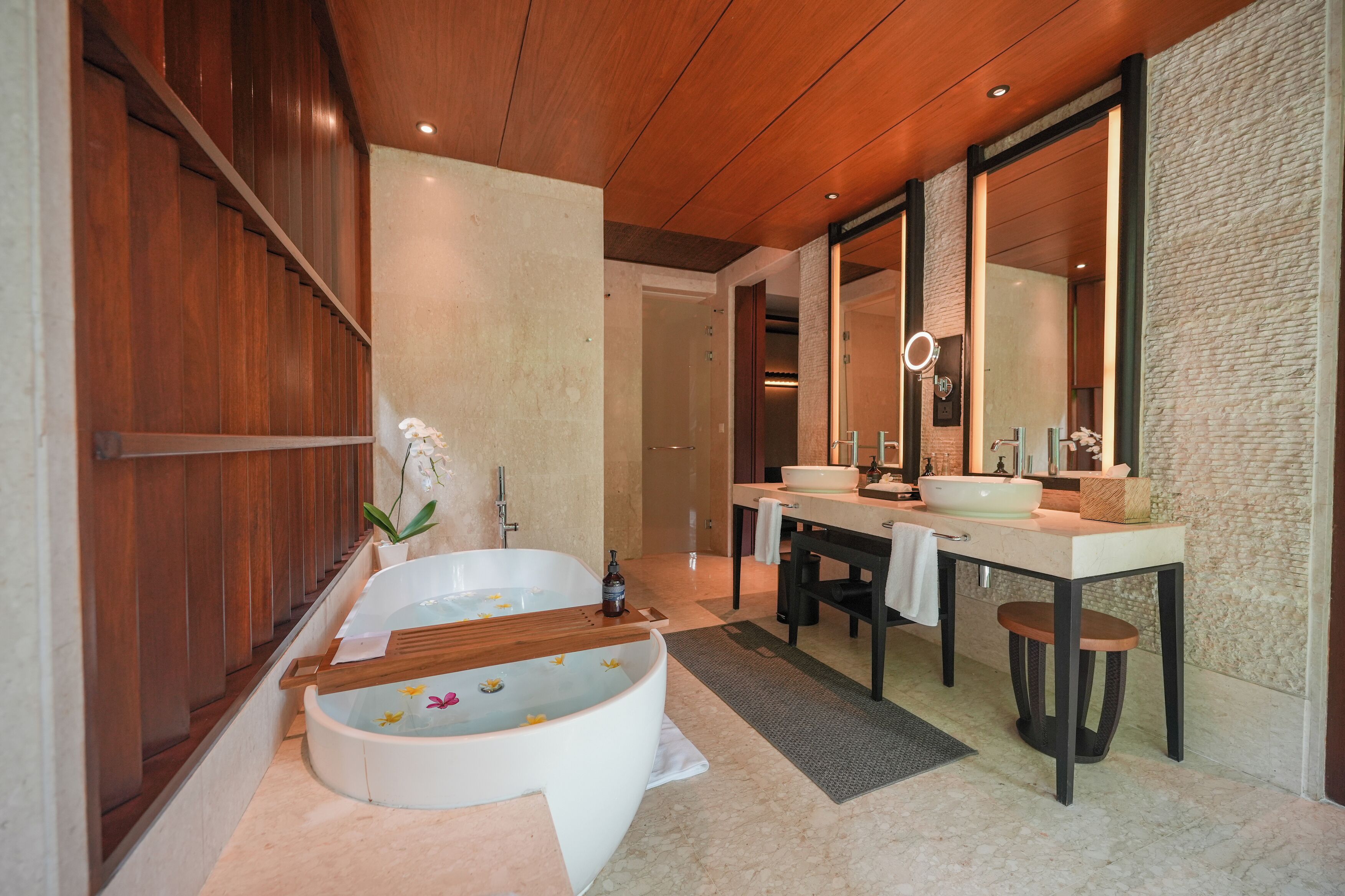 A modern bathroom with a freestanding bathtub, two sinks, a large mirror, and a wooden ceiling.