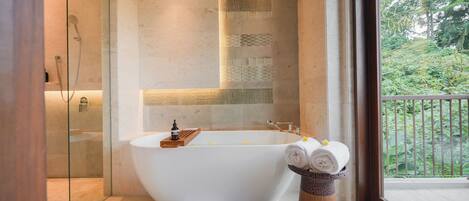 A modern bathroom with a freestanding bathtub, a glass shower enclosure, and a view of greenery through a large window.
