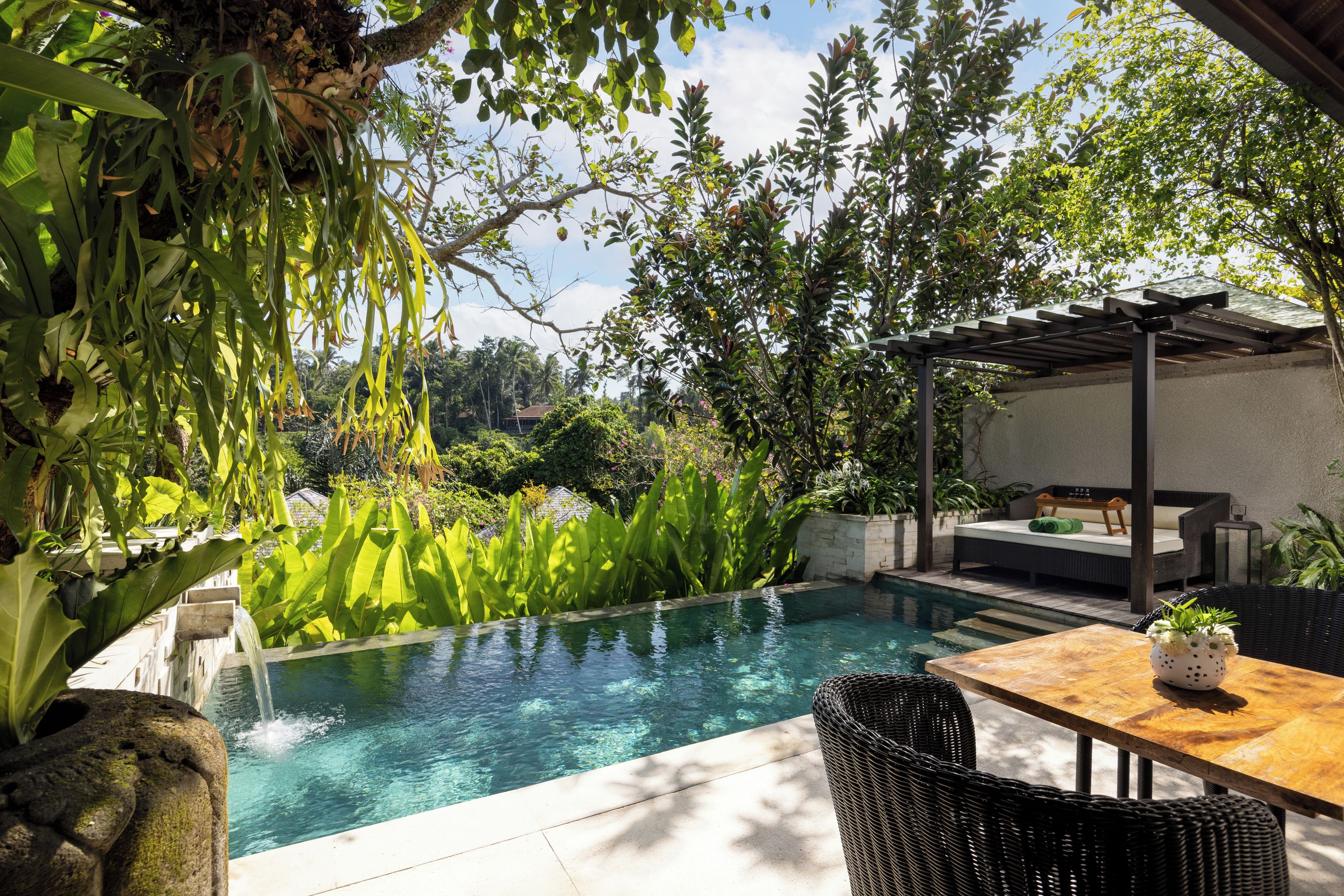 Ein Poolbereich mit Pergola, Sitzgelegenheiten und üppiger Bepflanzung.