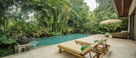 A poolside area with lounge chairs, a stone basin, and lush tropical vegetation.
