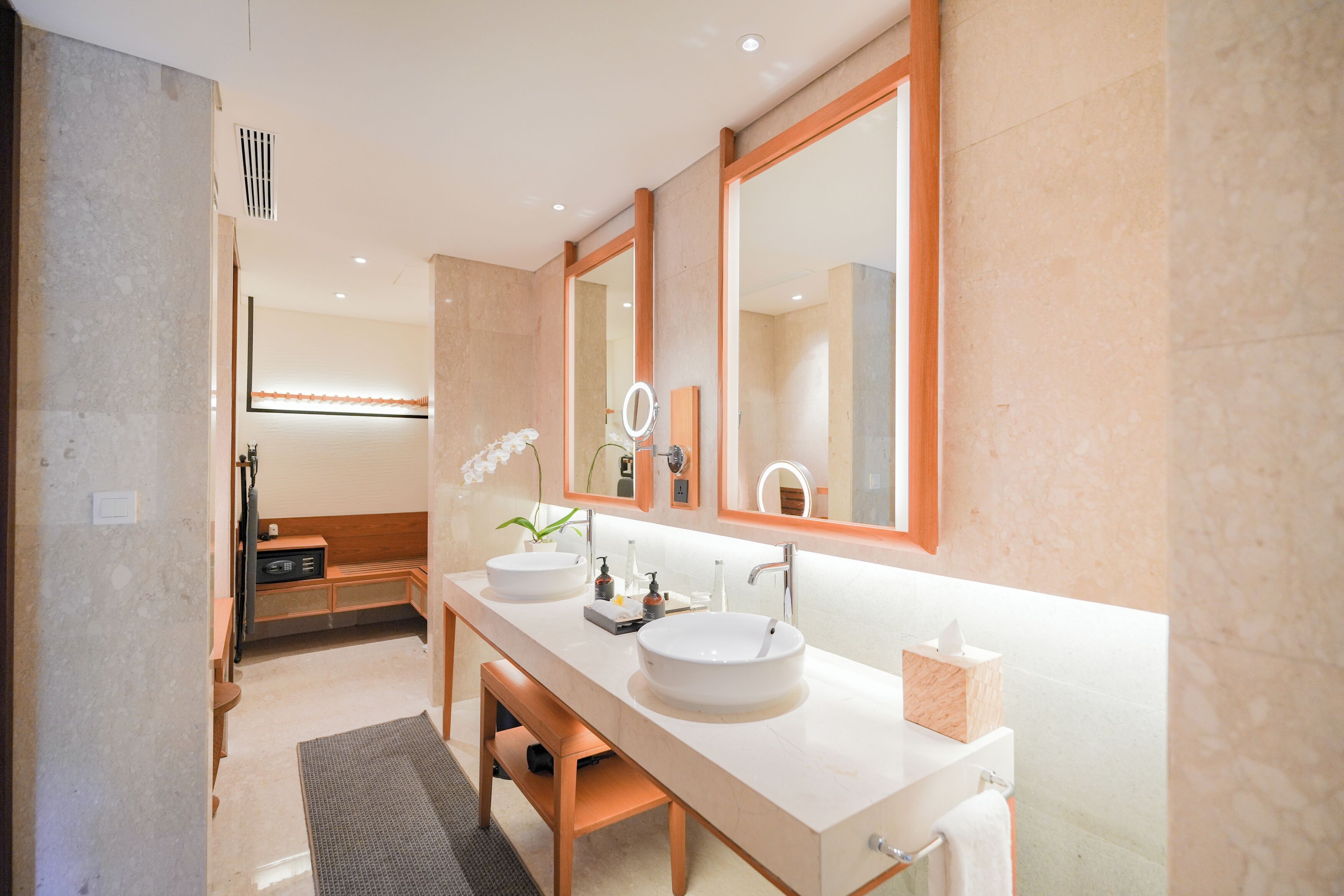 A modern bathroom with a long vanity, two sinks, a large mirror, and a bench.