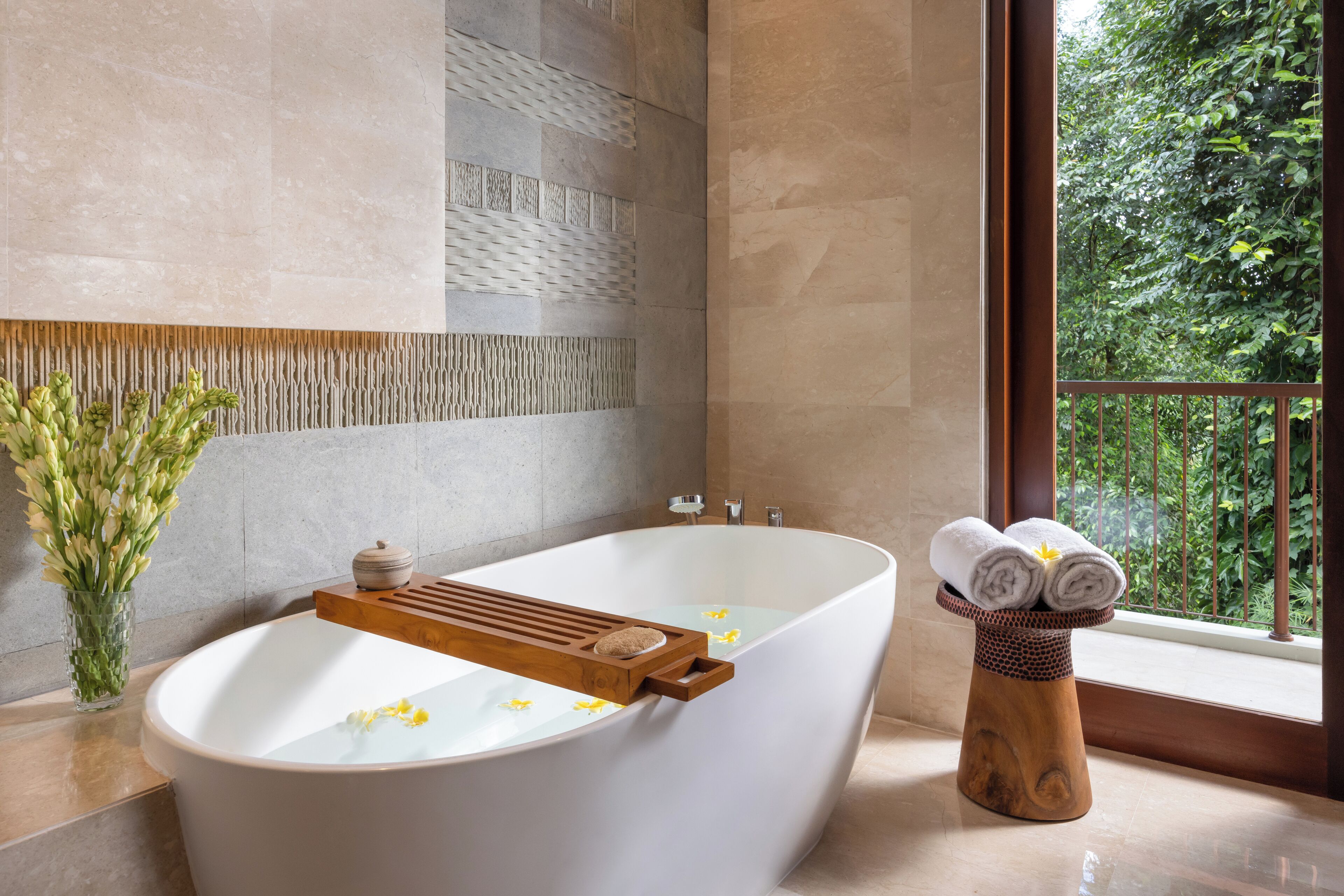 A modern bathroom with a freestanding bathtub, a wooden tray, and a vase of flowers.