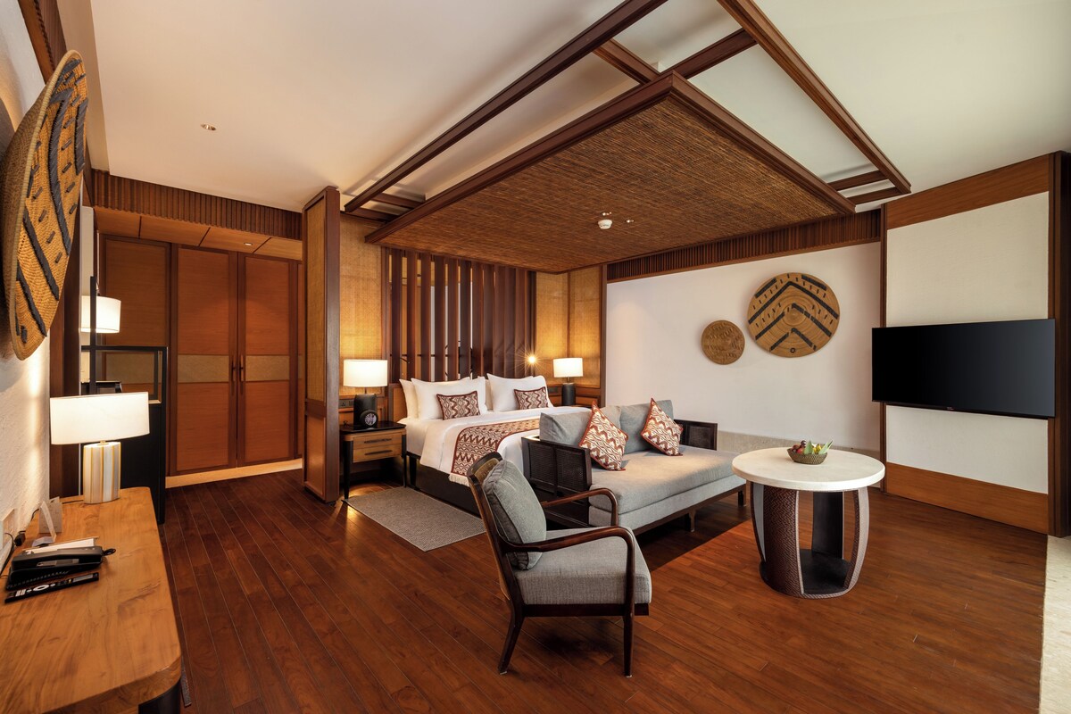 Quarto de hotel moderno com uma cama grande, um sofá, uma TV e uma pequena mesa.