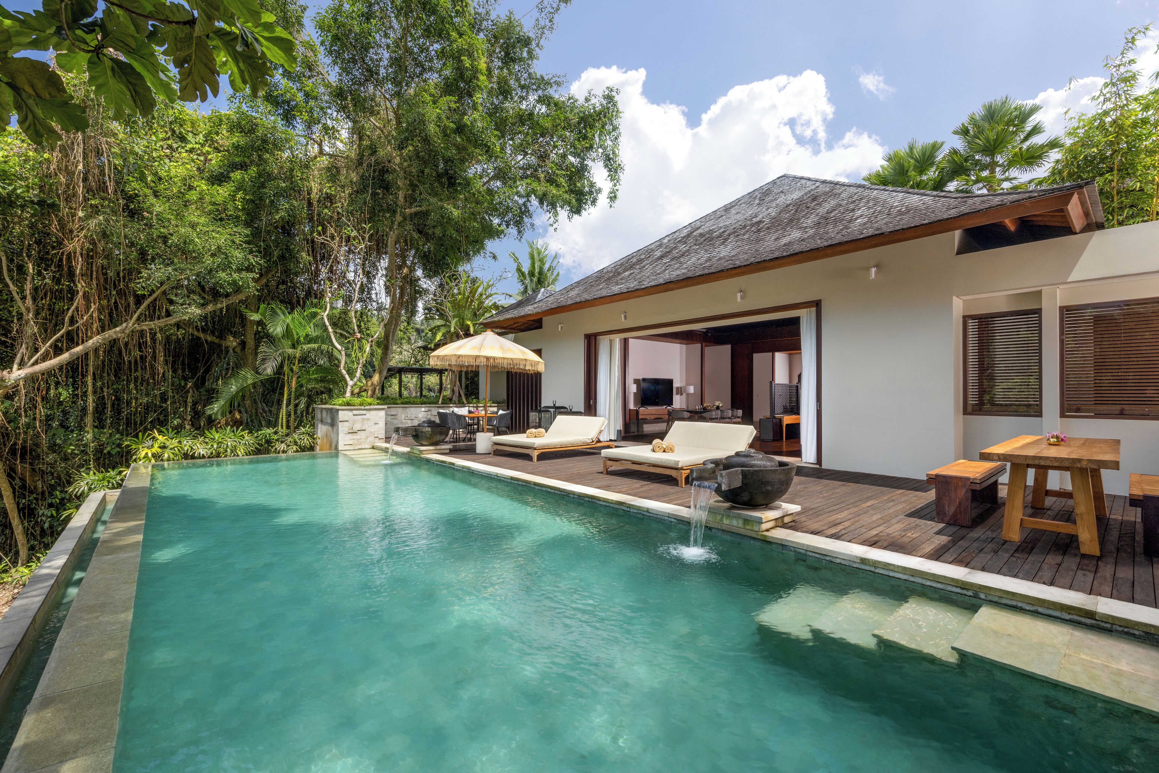 Un espace piscine extérieur moderne, avec des chaises longues, une terrasse en bois et une maison en arrière-plan.