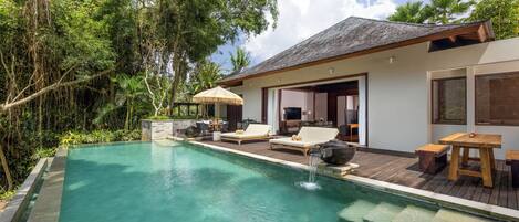 Un área de piscina exterior moderna con sillones de descanso, una terraza de madera y una casa al fondo.