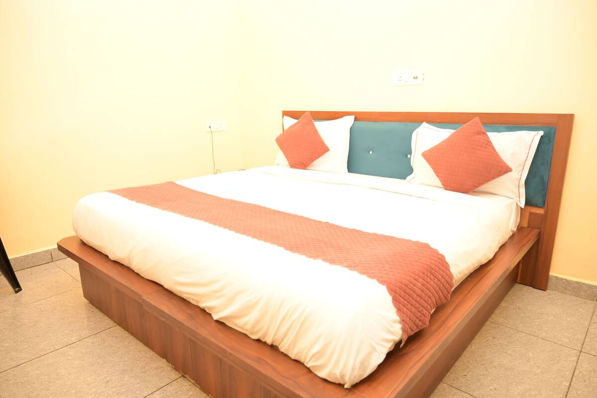 Uma cama com estrutura de madeira, roupa de cama branca e vermelha, e duas almofadas.