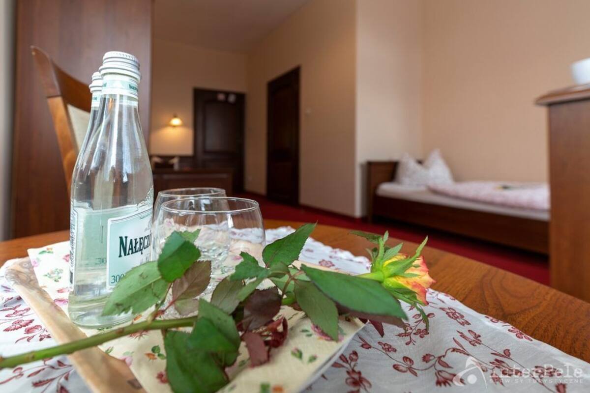 Habitación de hotel con una mesa de madera, una botella de agua, dos vasos y un mantel con motivos florales.