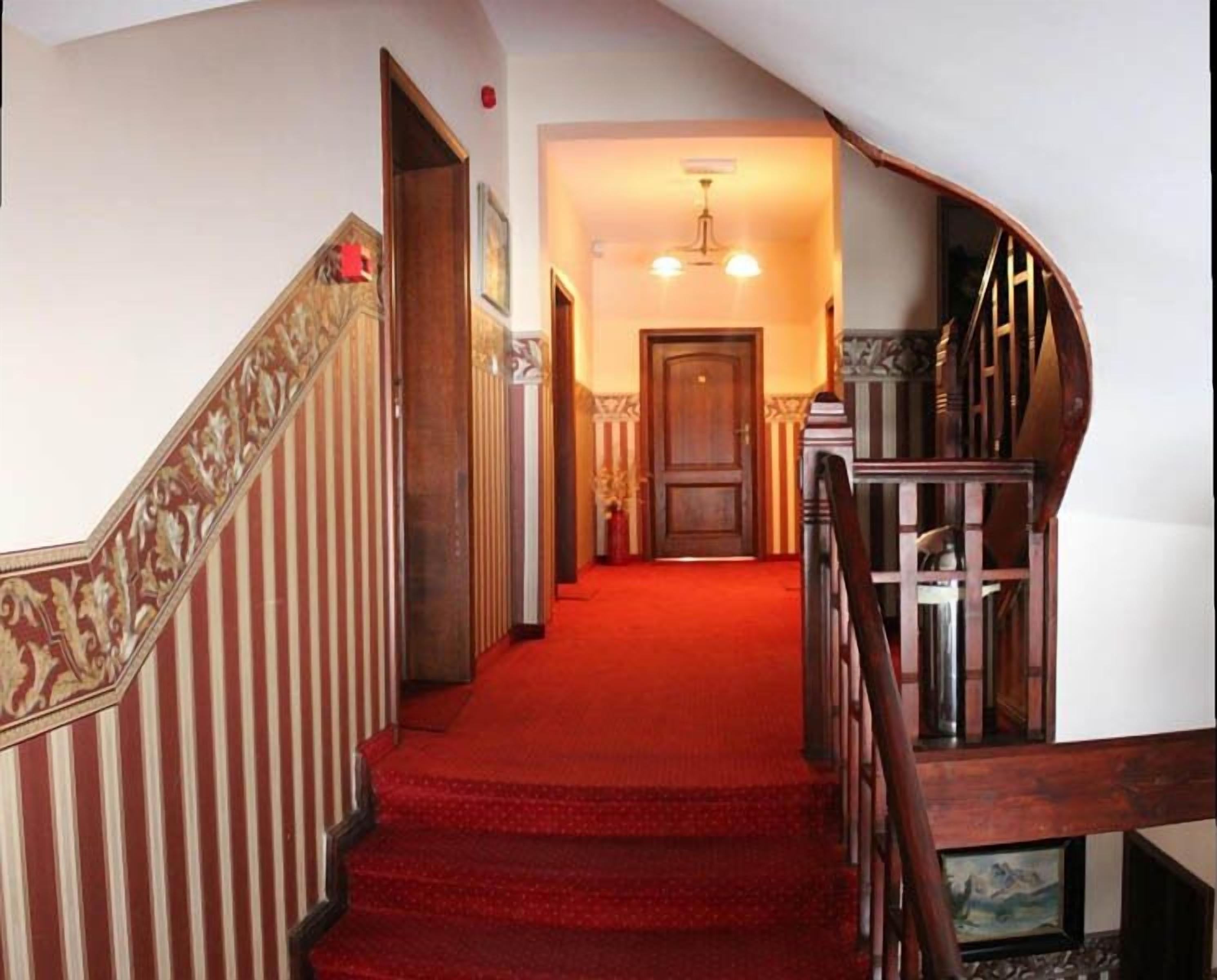 Una escalera con alfombra roja que conduce a una habitación con puerta de madera y un candelabro.