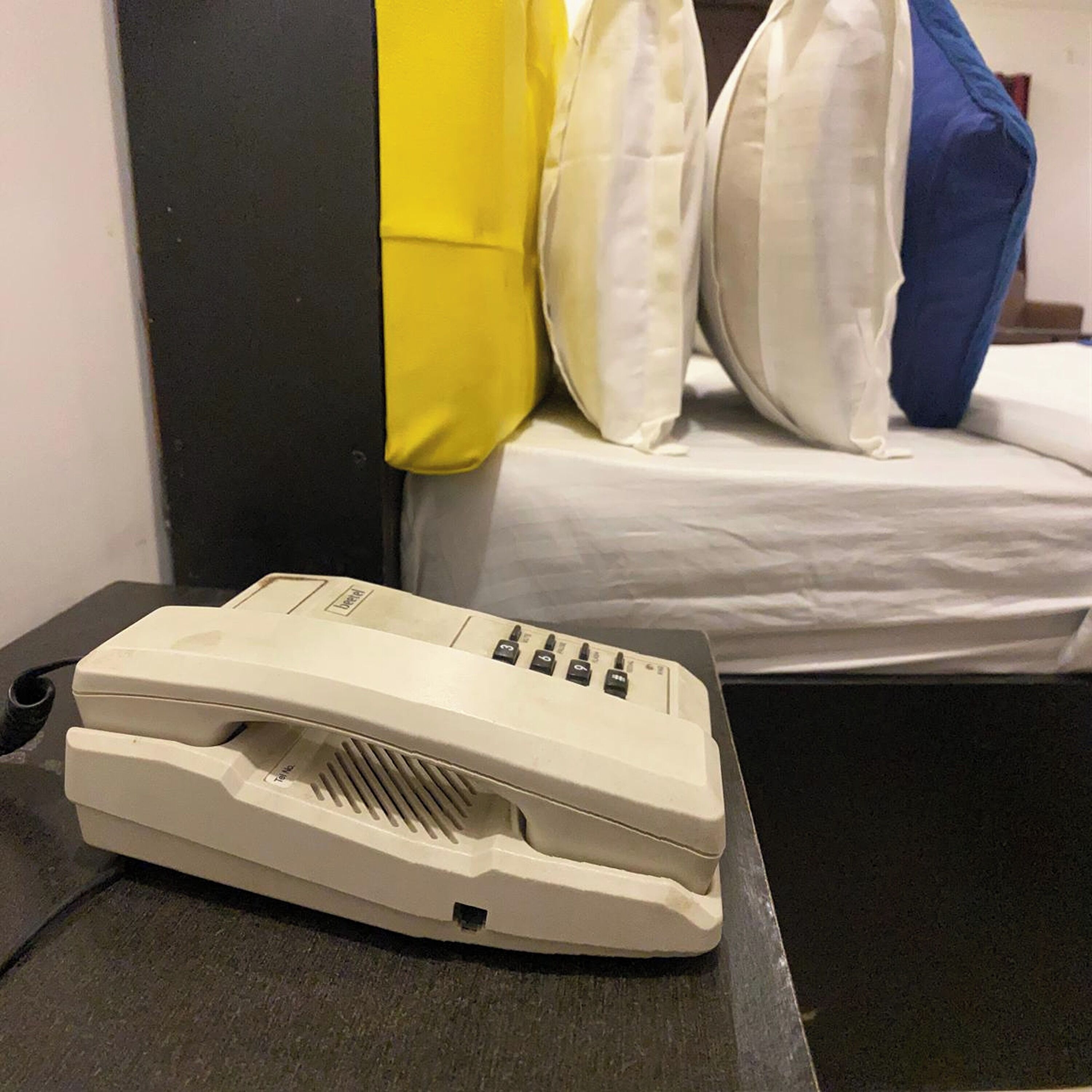 Una habitación con cama, almohadas y un fax sobre una mesa.