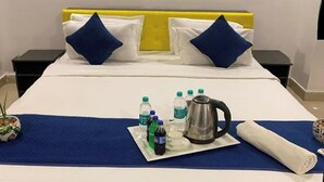 A neatly made bed with blue and white bedding, a blue throw blanket, and a tray with toiletries and a kettle. - Fortune Heights (Hyderabad)