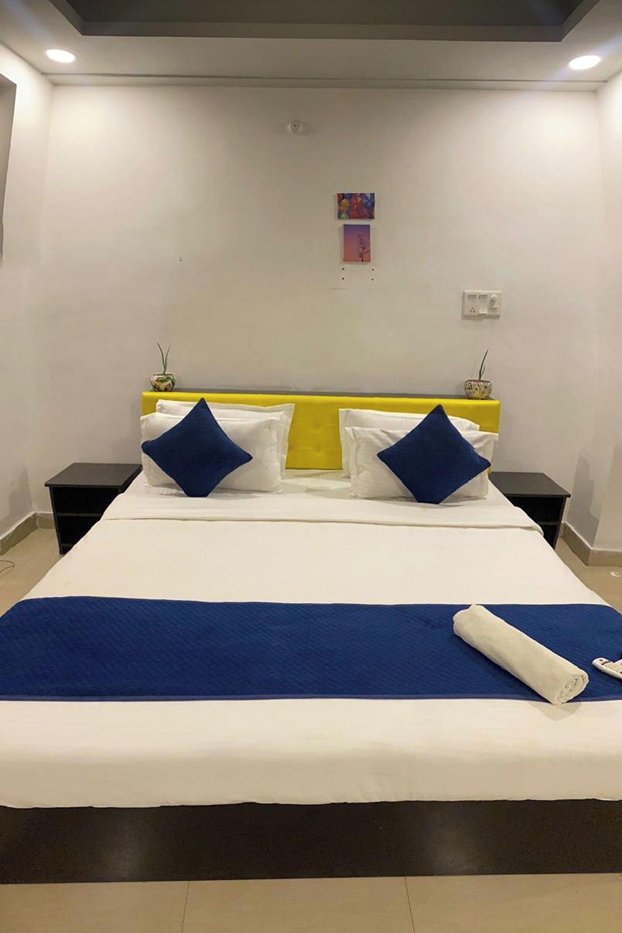 Une chambre d’hôtel avec un lit, deux tables de chevet, une tête de lit jaune et une couvre-lit bleue.