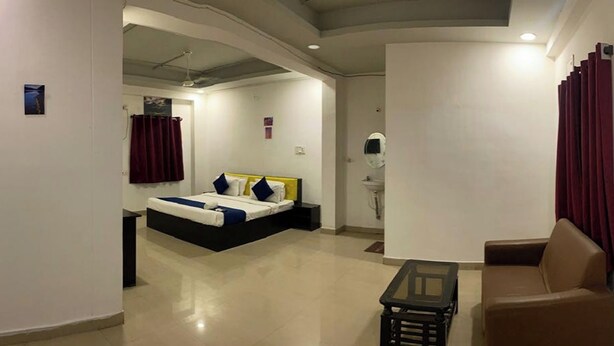 A modern hotel room with a bed, a sofa, a small table, and a bathroom with a mirror and sink. - Fortune Heights (Hyderabad)