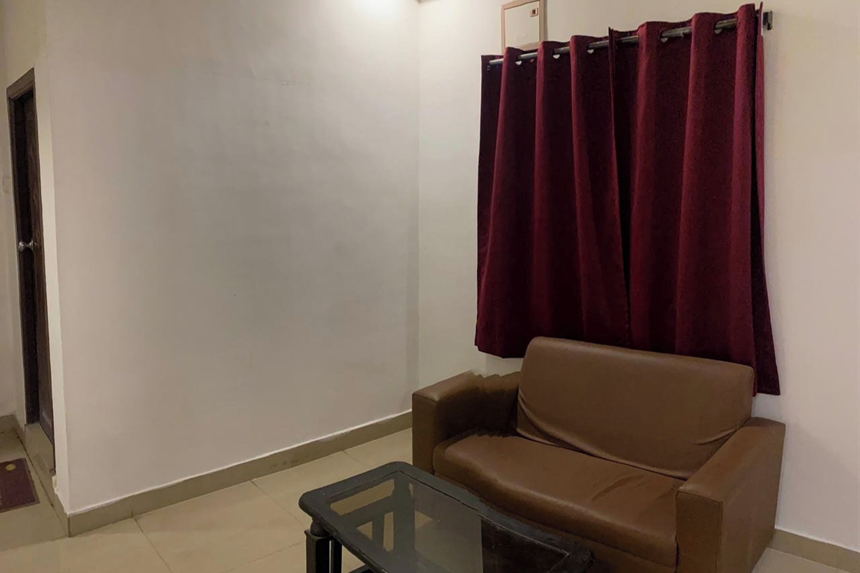 A living room with a brown leather sofa, a glass coffee table, and a red curtain.
