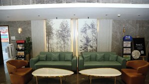 A lobby with two green sofas, two brown armchairs, and two white coffee tables. - Fortune Heights (Hyderabad)
