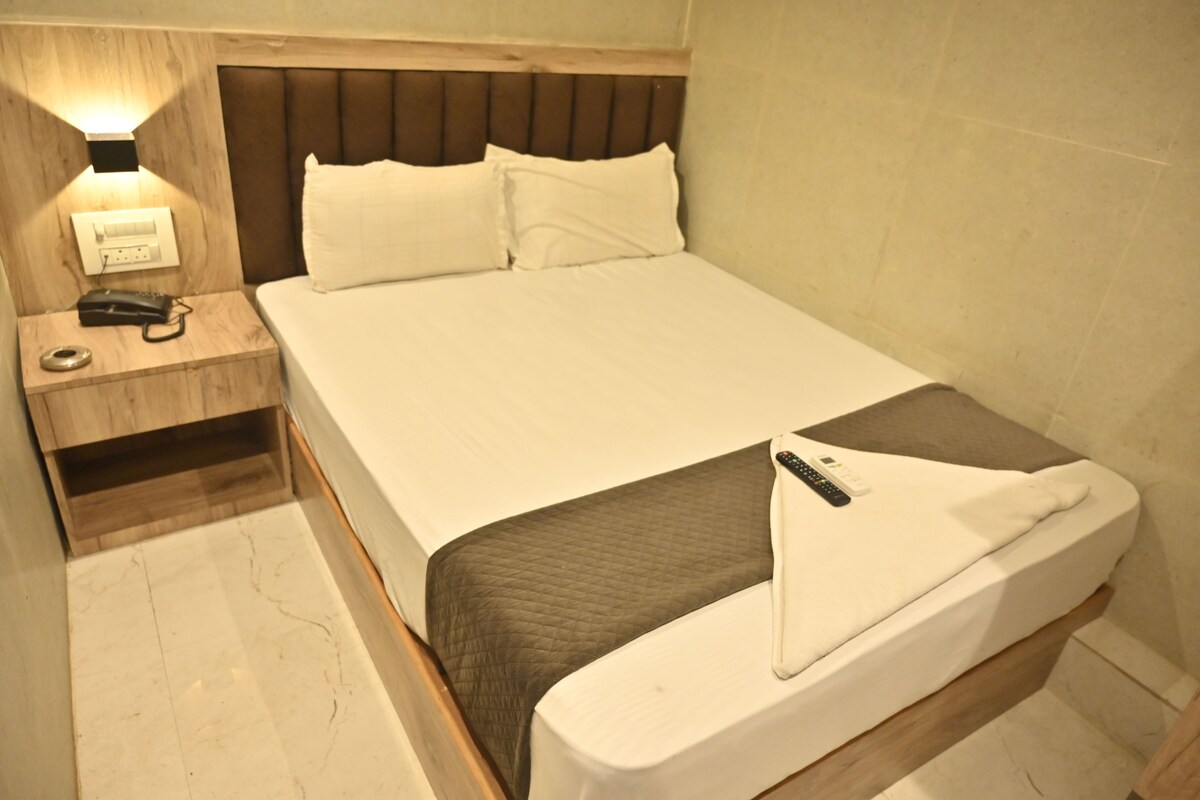 Une chambre d’hôtel avec un lit, une table de chevet avec un téléphone et une lampe, et un luminaire fixé au mur.