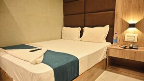 A neatly made bed with white and teal bedding, a wooden headboard, a bedside table with a lamp, and a wall socket.